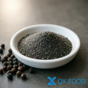 Pure black pepper powder BPP-K45 dark grey-black fine powder with lighter speckles in white ceramic sample dish on dark surface with whole black peppercorns scattered nearby