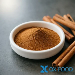 Pure cinnamon powder CP-K47 reddish-brown fine powder in white ceramic sample dish on dark surface with cinnamon sticks scattered nearby